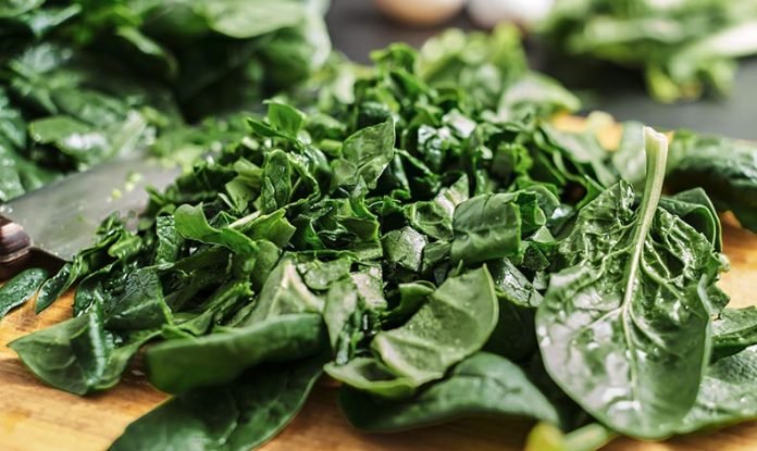 Juicy green sliced spinach leaves lie on a wooden cutting board.